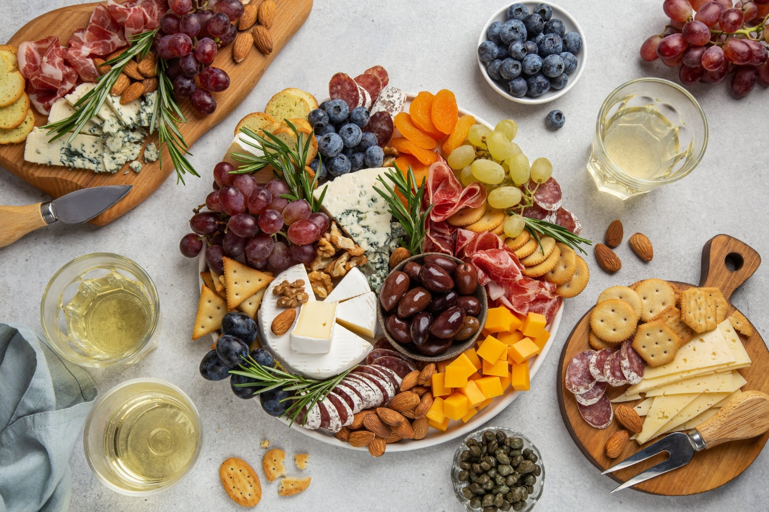 Charcuterie board with assortments of cheese, fruits, olives, crackers, herbs, and dried meat.