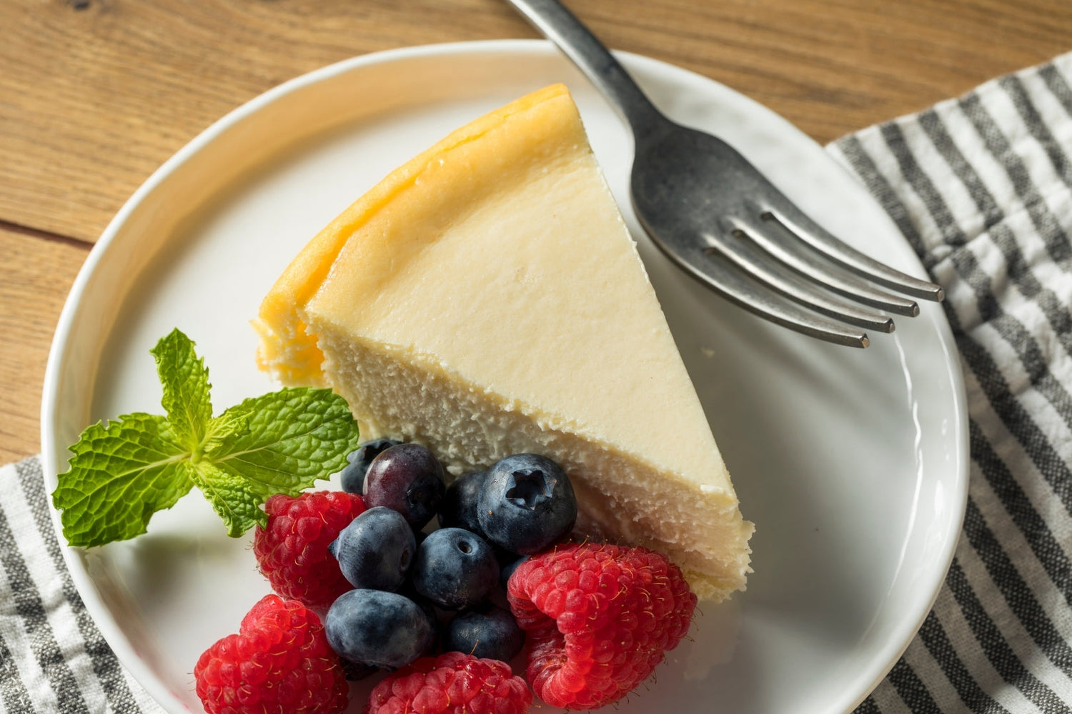 New York Cheesecake served on a plate with berries and mint