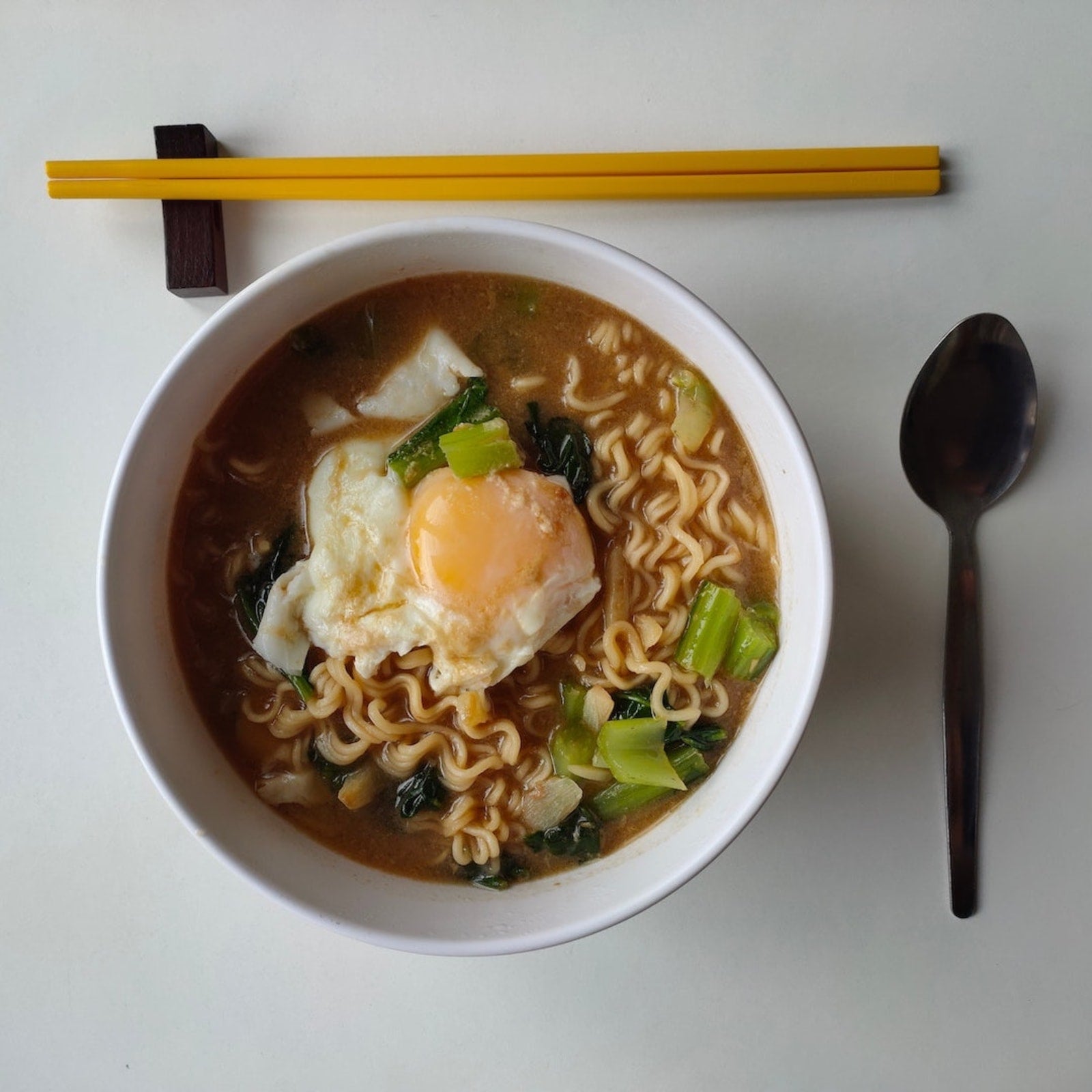 A bowl of LĒVO easy homemade ramen sits on a table next to a pair of chopsticks and a spoon.