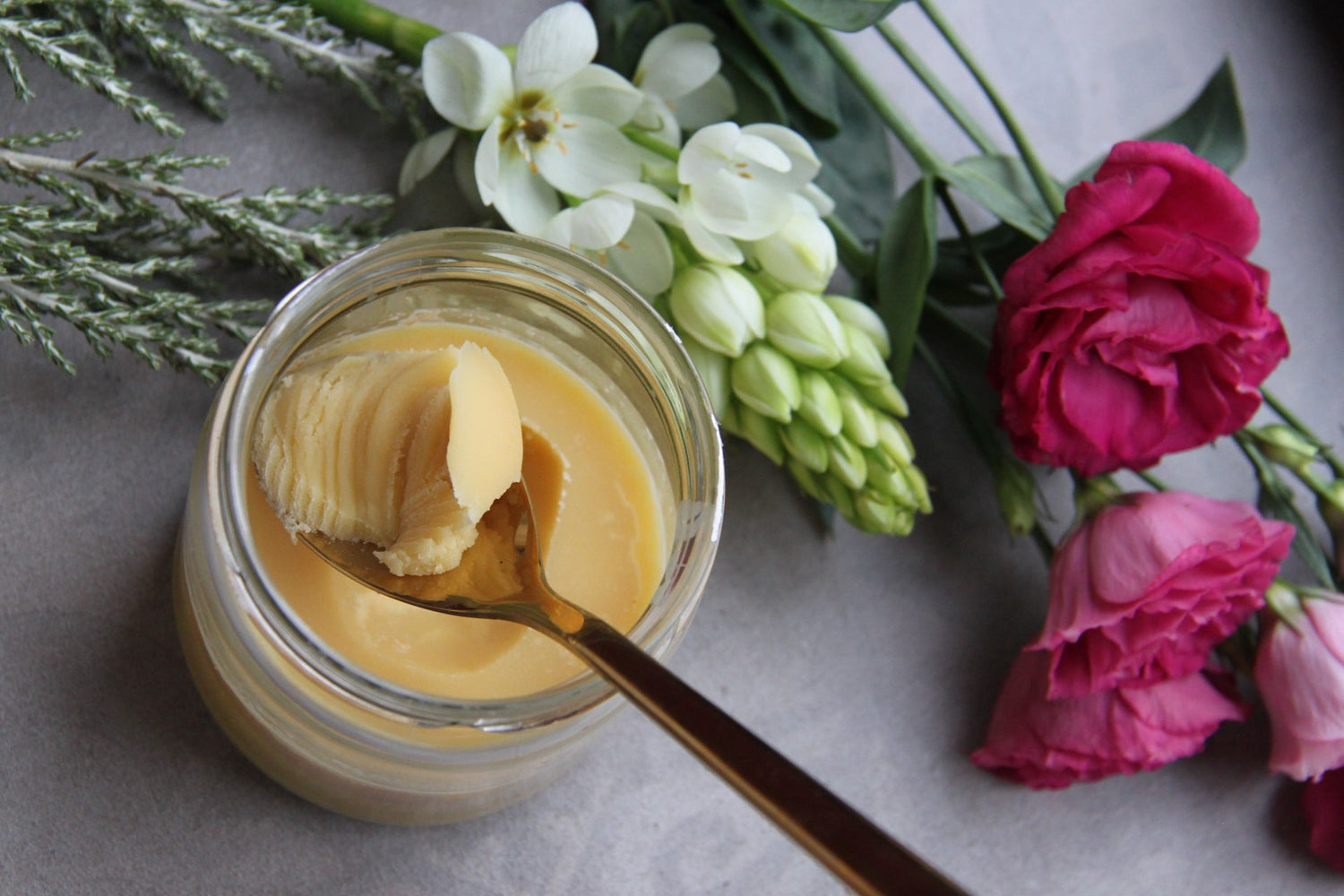 Image of lavender honey butter in a glass container next to flowers.