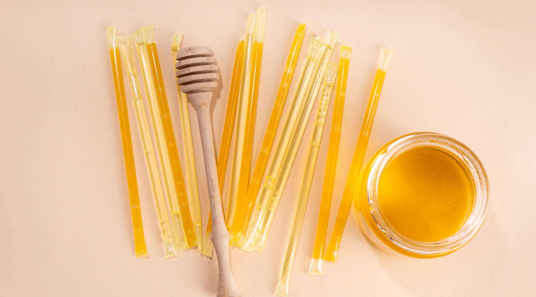 Golden flavored honey sticks, wooden honey wand, and jar of honey viewed from above.