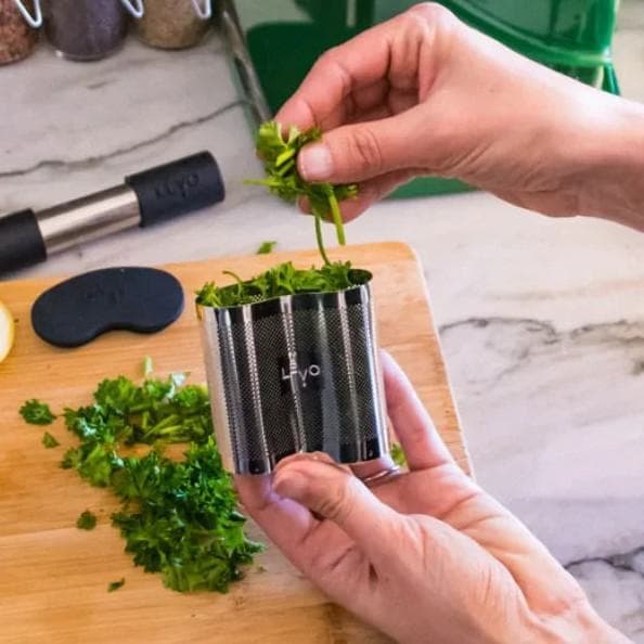 Packing fresh herbs into a LĒVO pod on a cutting board